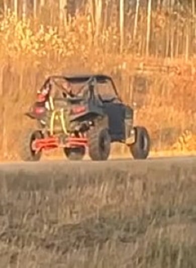A picture of a UTV driving away from the photographer in the fall, dead grass in the foreground and bare trees in the background.