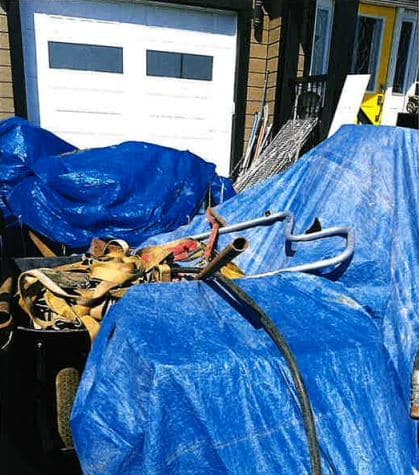 A photo of a pile of junk covered in blue tarps in front of a house with a garage.