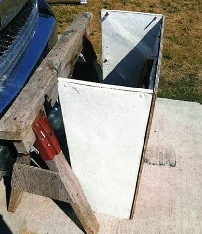 A photo of a wooden cupboard and a wooden saw horse sitting on concrete.