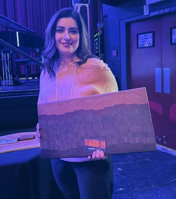A woman holding a wooden cutting board she won.