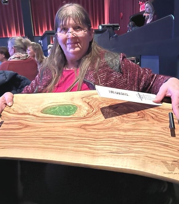 A woman holding a wooden cutting board she won.