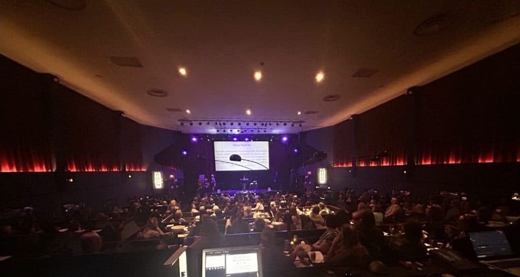 A group of people in a theatre watching a PowerPoint presentation.