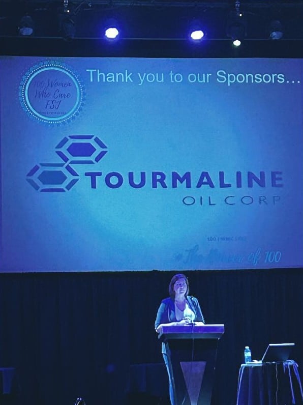 A lady standing in front of a screen with "Tourmaline Oil Corp" on it.