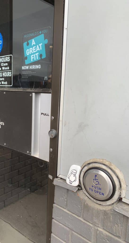 A picture of a door to a business with a painted rock of Baymax leaning against the push to open button.