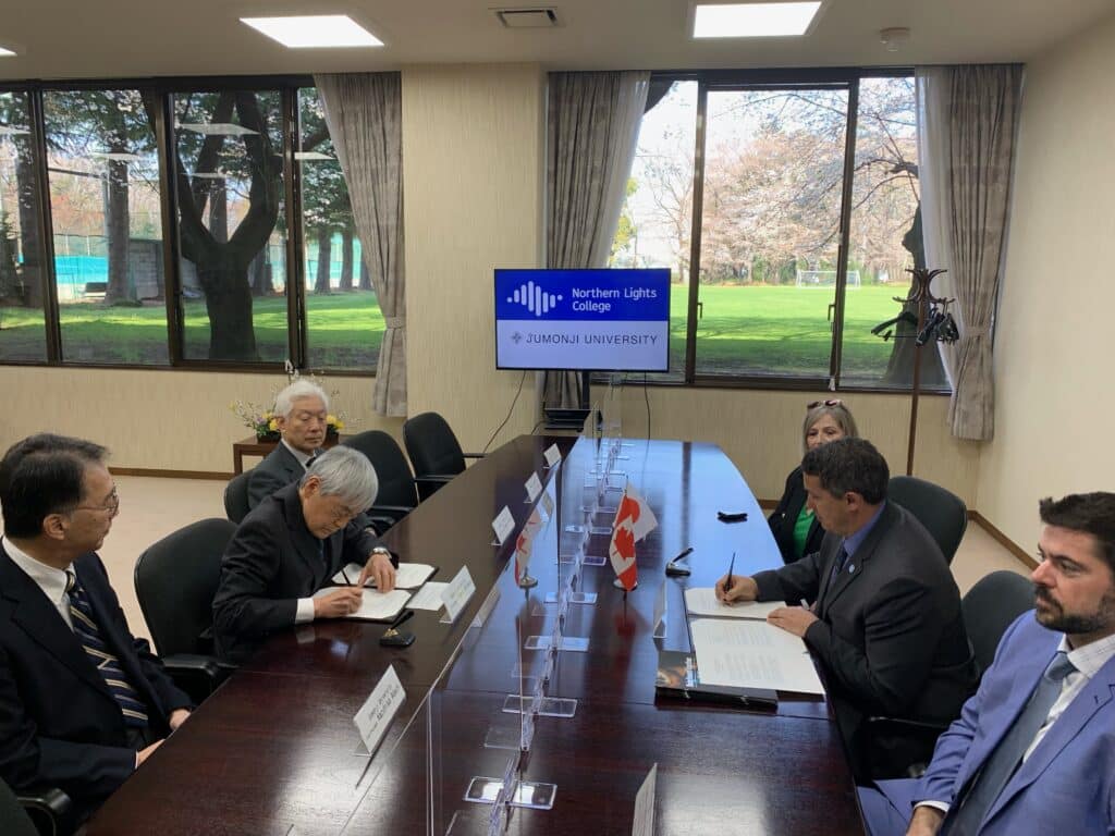 A group of six sitting at a long table to sign documents