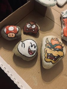 Rocks painted as a one up mushroom, Boo, Bowser and other Mario characters in a cardboard box.