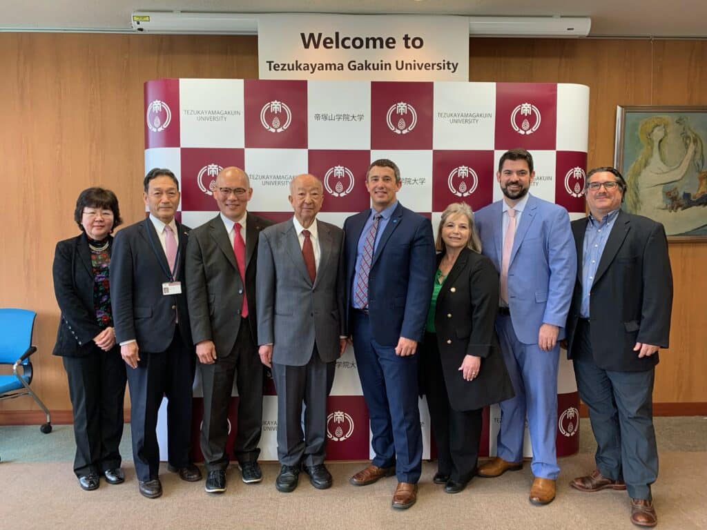 A group of people standing in front of a sign that reads "Welcome to Tezukayama Gakuin University."