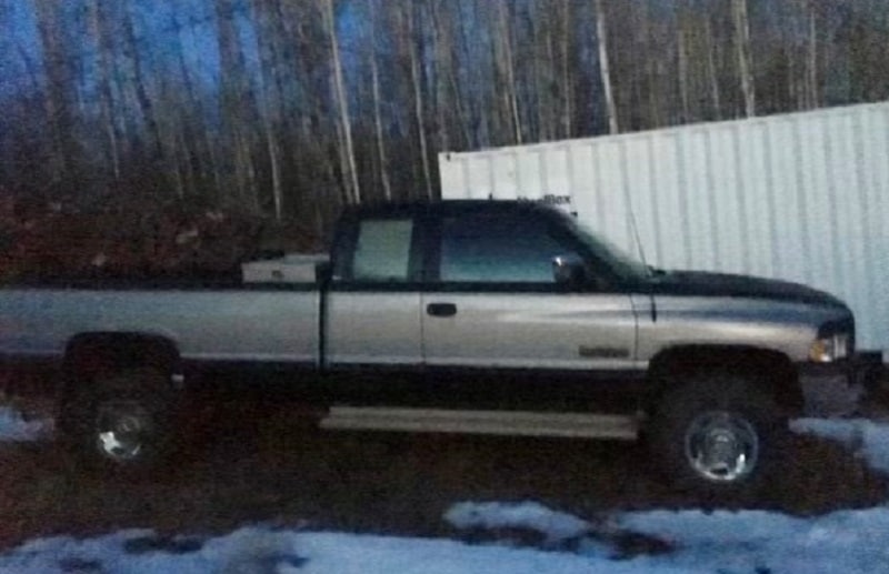 A green and grey dodge truck in front of a white storage container.