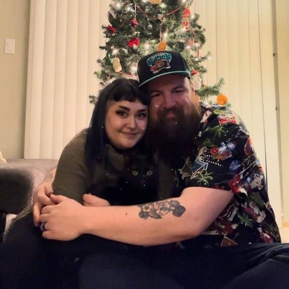Two people and a cat in front of a Christmas tree